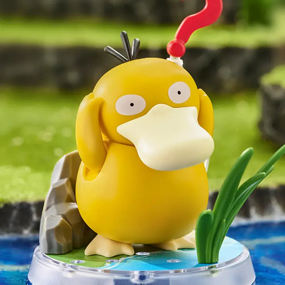 Yellow duck-like figurine with a red antenna on a clear base with a green grass background